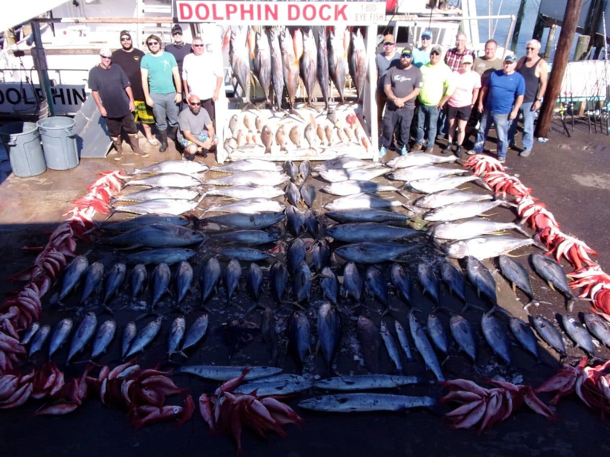 A crew of anglers standing behind rows of tuna, snapper and wahoo on the dock