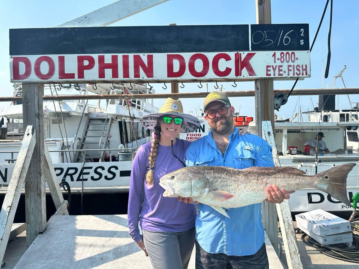Two anglers holding a bull red drum in front of the Dolphin Express